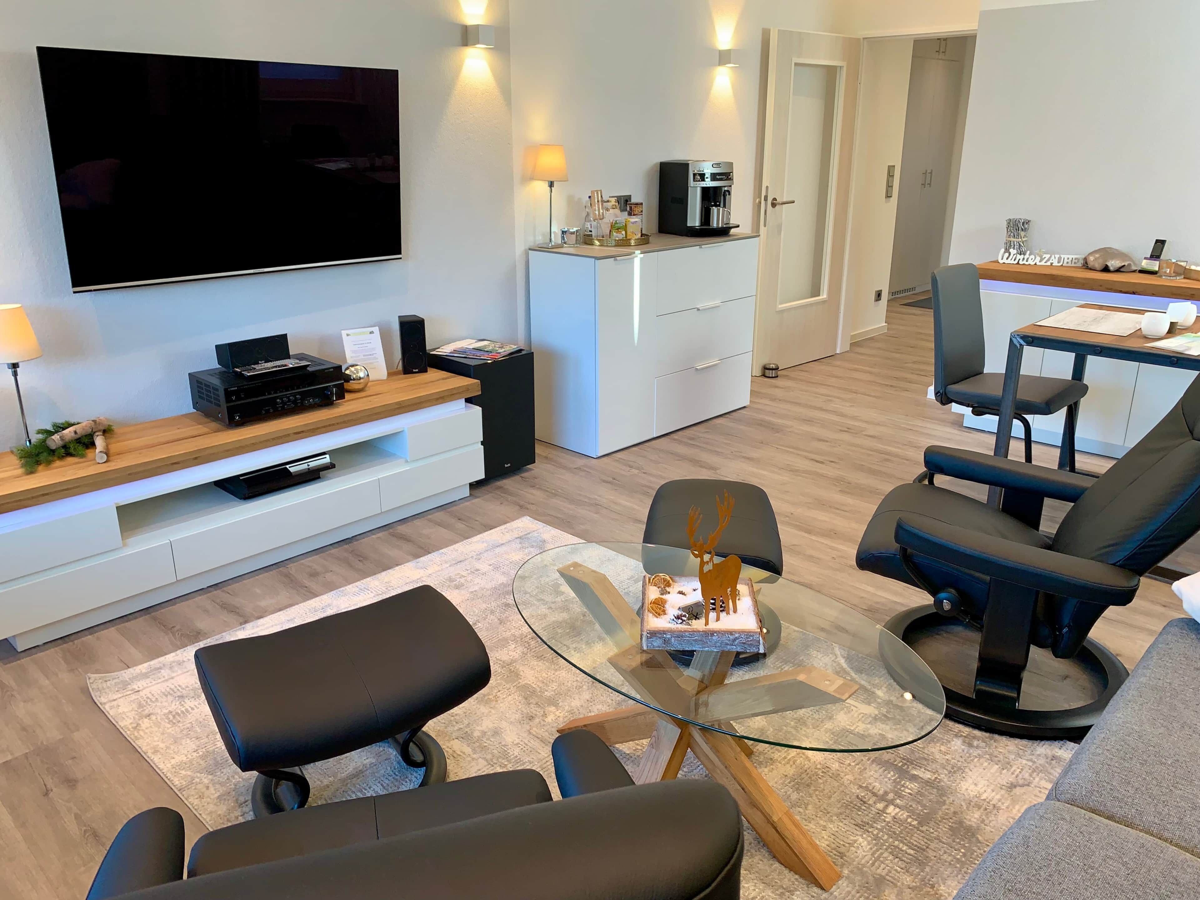 A modern living room with a flat-screen TV, a coffee machine, and a glass-top coffee table.