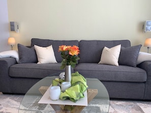 Ein modernes Wohnzimmer mit einem grauen Sofa, einem Glastisch und einer Vase mit Blumen.
