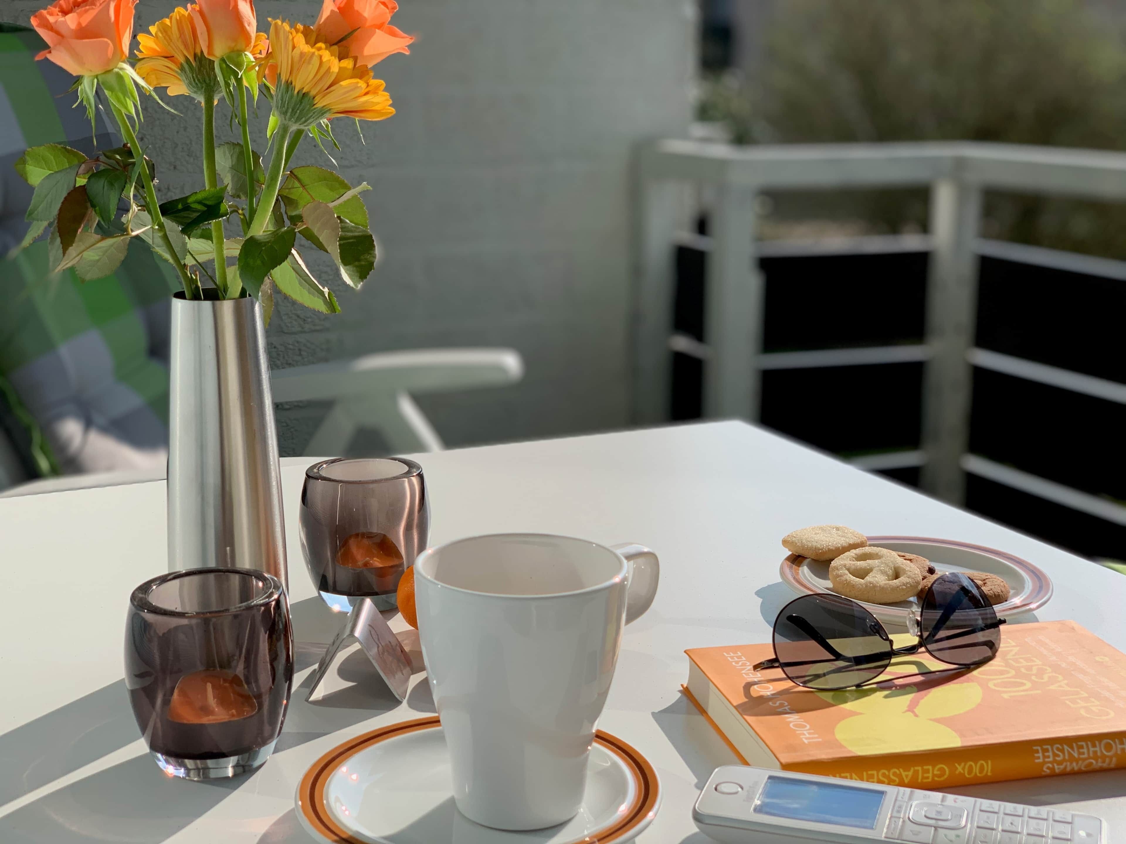 Ein Tisch mit Blumen in einer Vase, einer Tasse, einem Glas, einem Buch und Keksen.