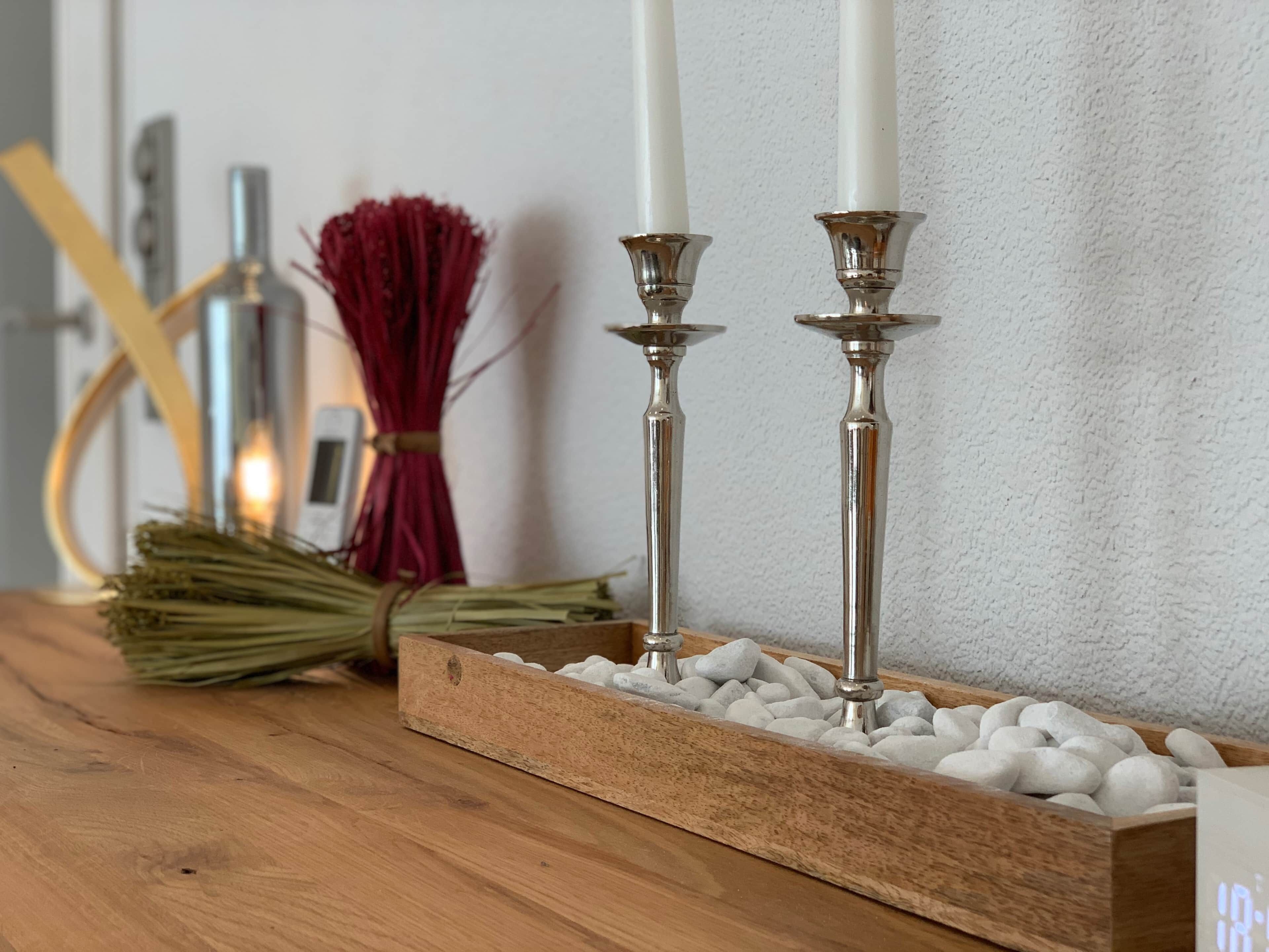 Une table en bois, ornée de deux chandeliers et d’une bougie, d’un bouquet rouge et d’un petit appareil électronique.