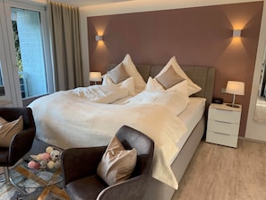 Ein modernes Schlafzimmer mit einem großen Bett, zwei Nachttischen, einem Sessel und einem Glastisch.