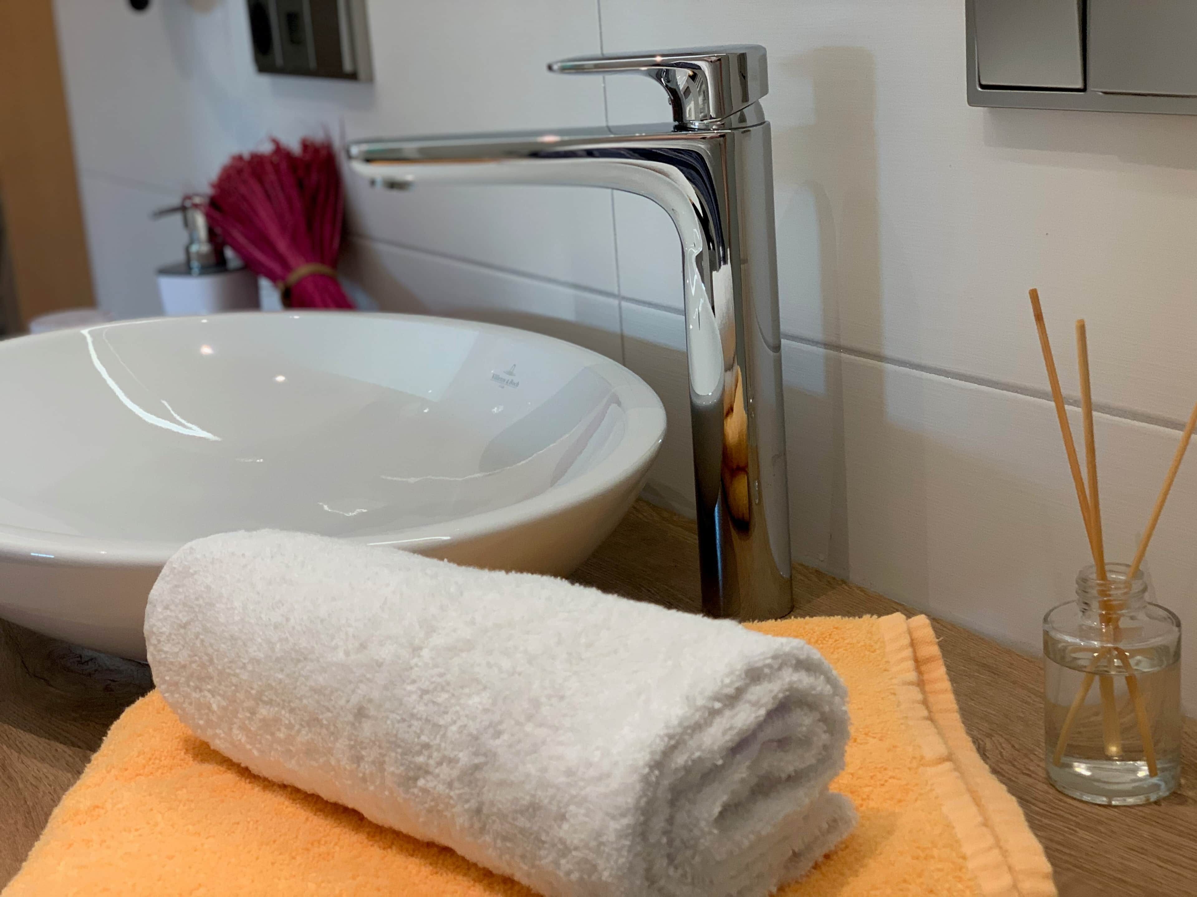 Een badkamer met een witte wastafel, een handdoek en een glazen pot met rietstelen.