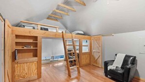 Quarto estilo loft com escada de madeira, uma poltrona de couro preta e vista para o céu.