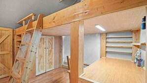 Um quarto com cama em mezzanine, escada de madeira e prateleiras embutidas.