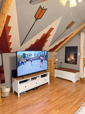 A living room with a television, wooden flooring, a bench, and a ceiling with geometric patterns. - Historic Old Town Attic Loft—Steps from Albuquerque’s Best Sights (Albuquerque)