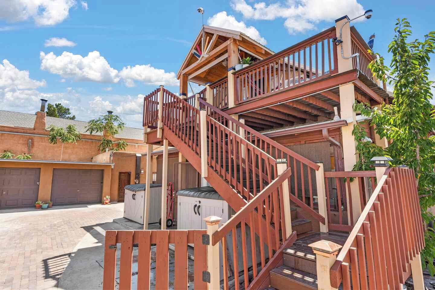 A multi-level wooden structure with a staircase, outdoor seating area, and a fenced patio.