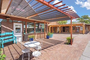 Un'area patio esterna con una zona salotto coperta, un tavolo e sedie, e piante in vaso.