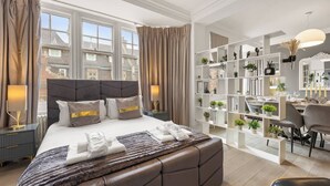 Ein modernes Hotelzimmer mit einem großen Bett, einer Sitzecke mit einem Sessel und einem Bücherregal mit Büchern und Pflanzen.