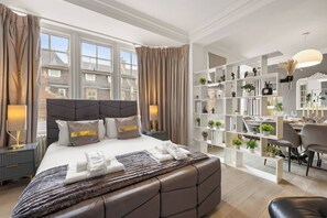 Ein modernes Hotelzimmer mit einem großen Bett, einer Sitzecke mit einem Sessel und einem Bücherregal mit Büchern und Pflanzen.