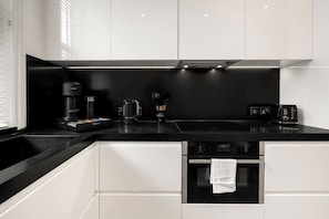 Eine moderne Küche mit schwarzem Arbeitsplatz, weißen Schränken, einer Kaffeemaschine, einem Wasserkocher und einem Toaster.