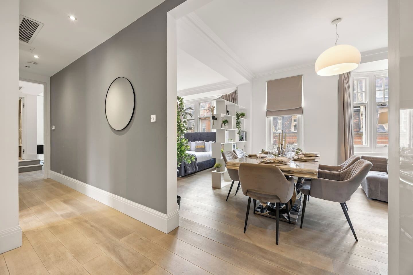 A modern dining area with a round mirror, a dining table set for four, and a hanging light fixture.