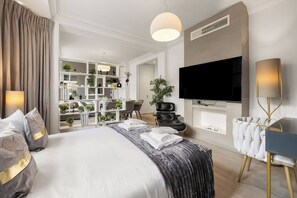 A modern hotel room with a large bed, a TV mounted on the wall, a seating area with a chair, and a plant. - The Duke Residence / 3Bed 2.5Bath in Mayfair (Greater London)