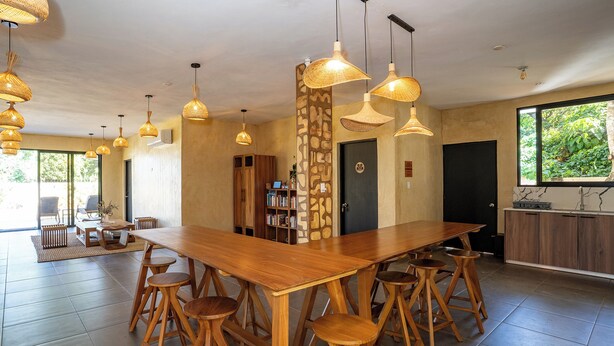 A spacious dining area with a long wooden table and multiple stools, surrounded by hanging pendant lights.