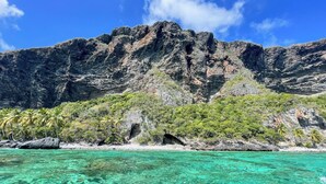 A coastal landscape with clear turquoise waters, rocky cliffs, and dense vegetation.