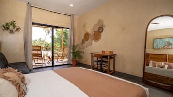A bedroom with a bed, a desk, and a chair. There is a balcony with a view of trees.