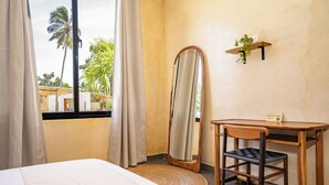 A hotel room with a bed, a desk, a mirror, and a window with curtains.