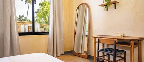 Ein Hotelzimmer mit Bett, Schreibtisch, Spiegel und einem Fenster mit Vorhängen.