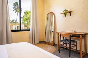 A hotel room with a bed, a desk, a mirror, and a window with curtains.