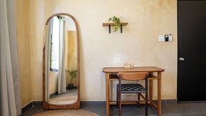 A room with a wooden table, a chair, a mirror, a small shelf with a plant, and a door.