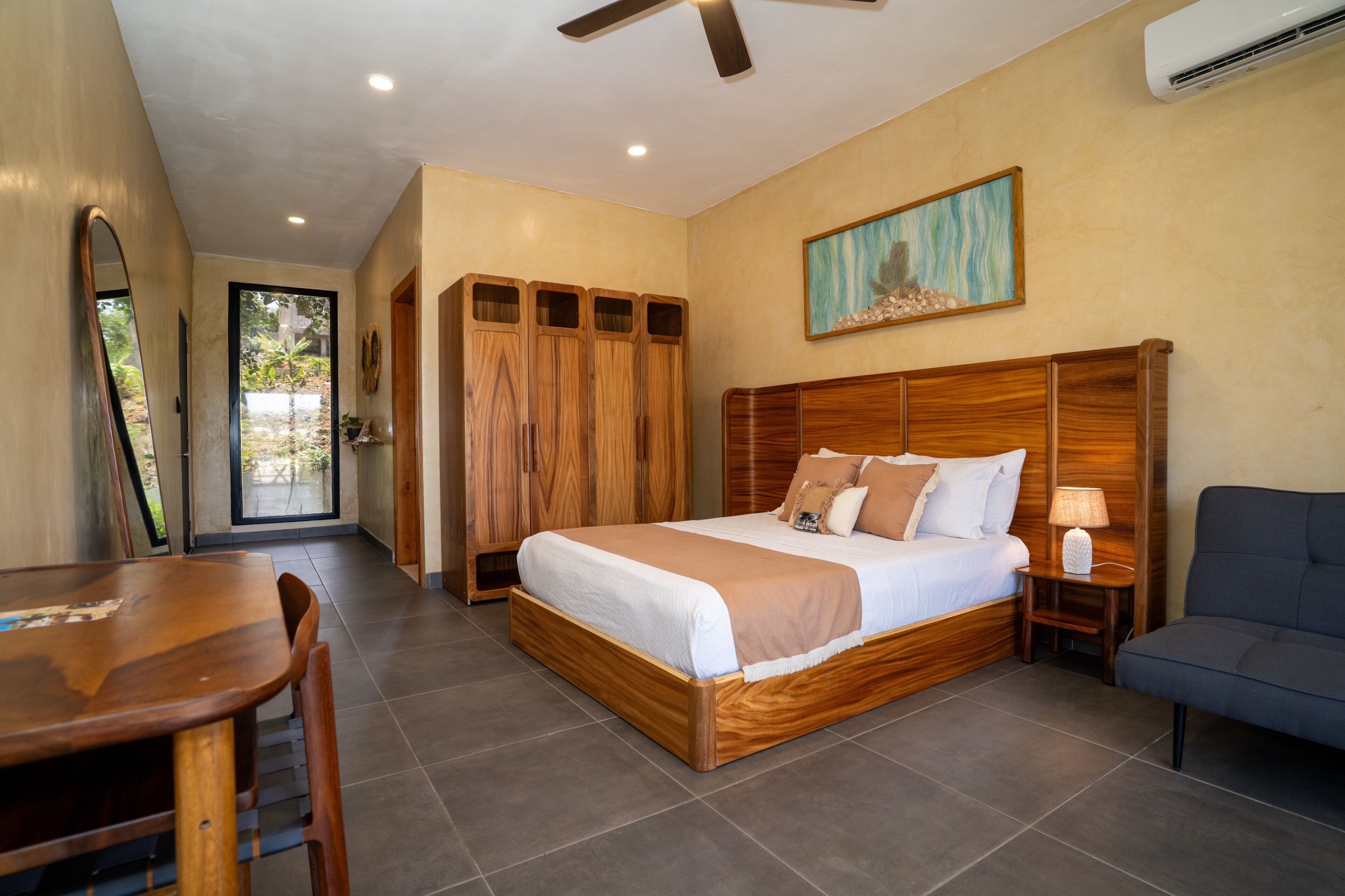 A bedroom with a wooden bed, a desk, a chair, a wardrobe, and a painting on the wall.