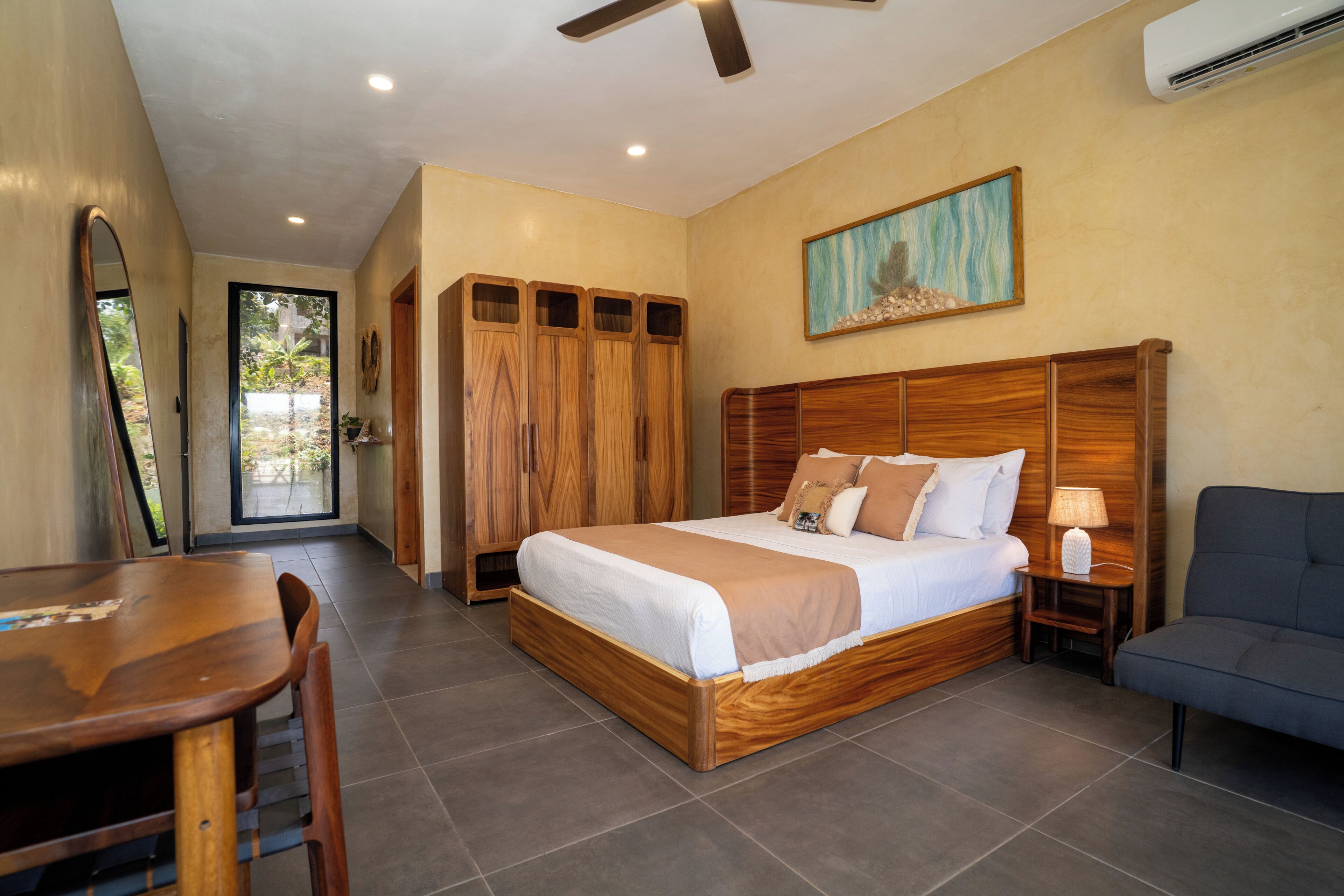 A bedroom with a wooden bed, a desk, a chair, a wardrobe, and a painting on the wall.