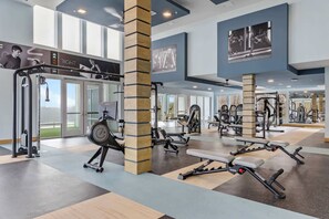 Een sportschool met diverse trainingsapparaten, grote ramen en uitzicht op het buiten.
