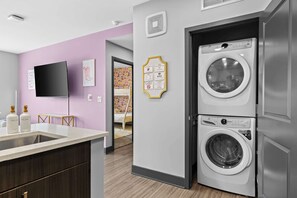 Een moderne wasruimte met een voorlader wasmachine en droger, een wasbak en een flatscreen televisie aan de muur.