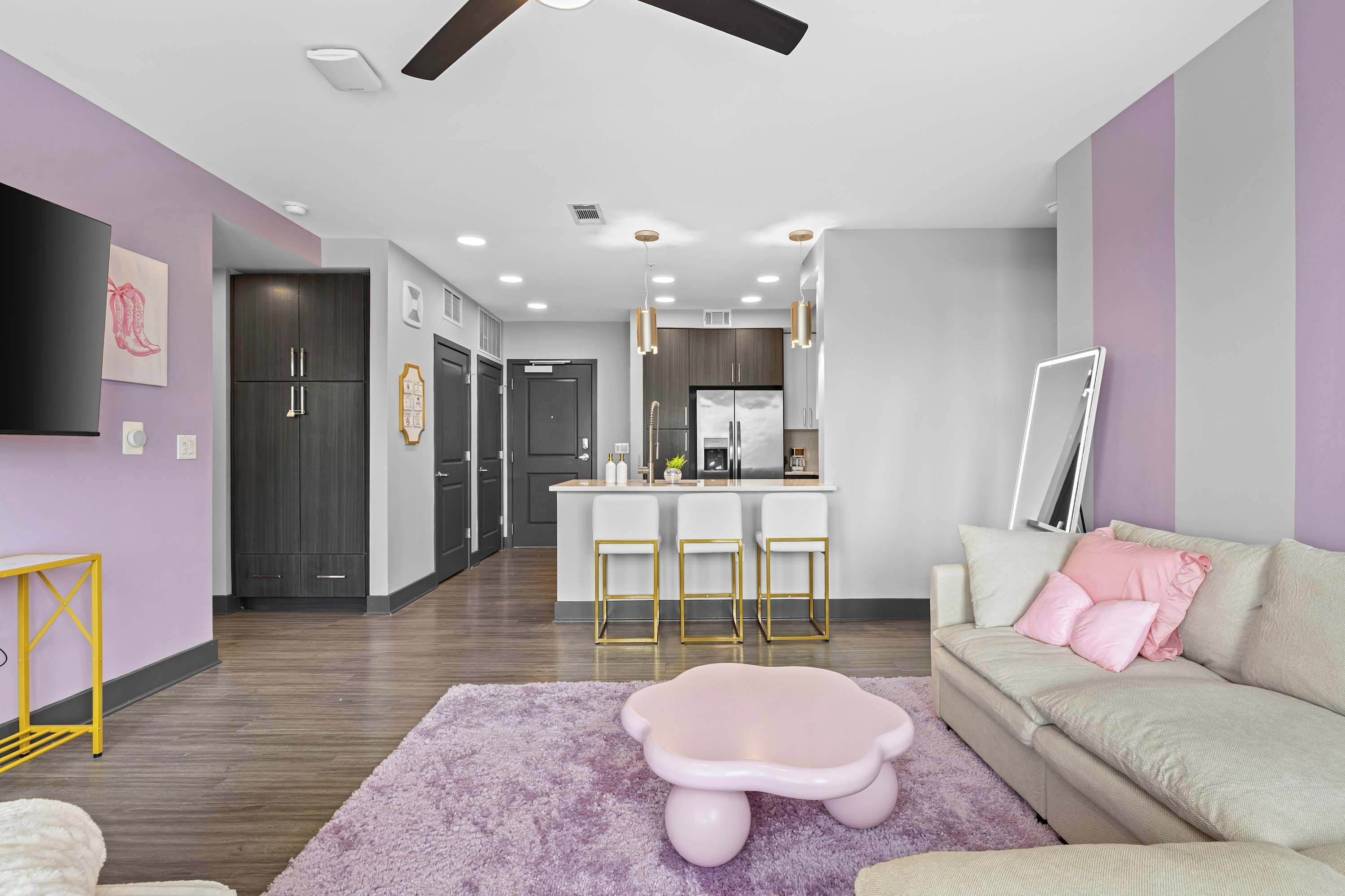 Una sala moderna con un sofá, un taburete rosa y una zona de cocina con barra.