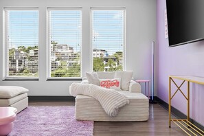 A modern living room with a sofa, a pink rug, and a TV mounted on the wall. - Vibrant Nashville Retreat, Pool and Glam Room (Nashville)