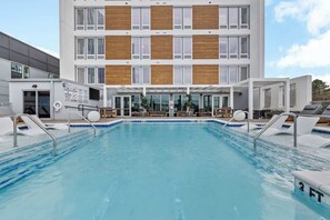A swimming pool with lounge chairs and a building with multiple floors and large windows. - Vibrant Nashville Retreat, Pool and Glam Room (Nashville)