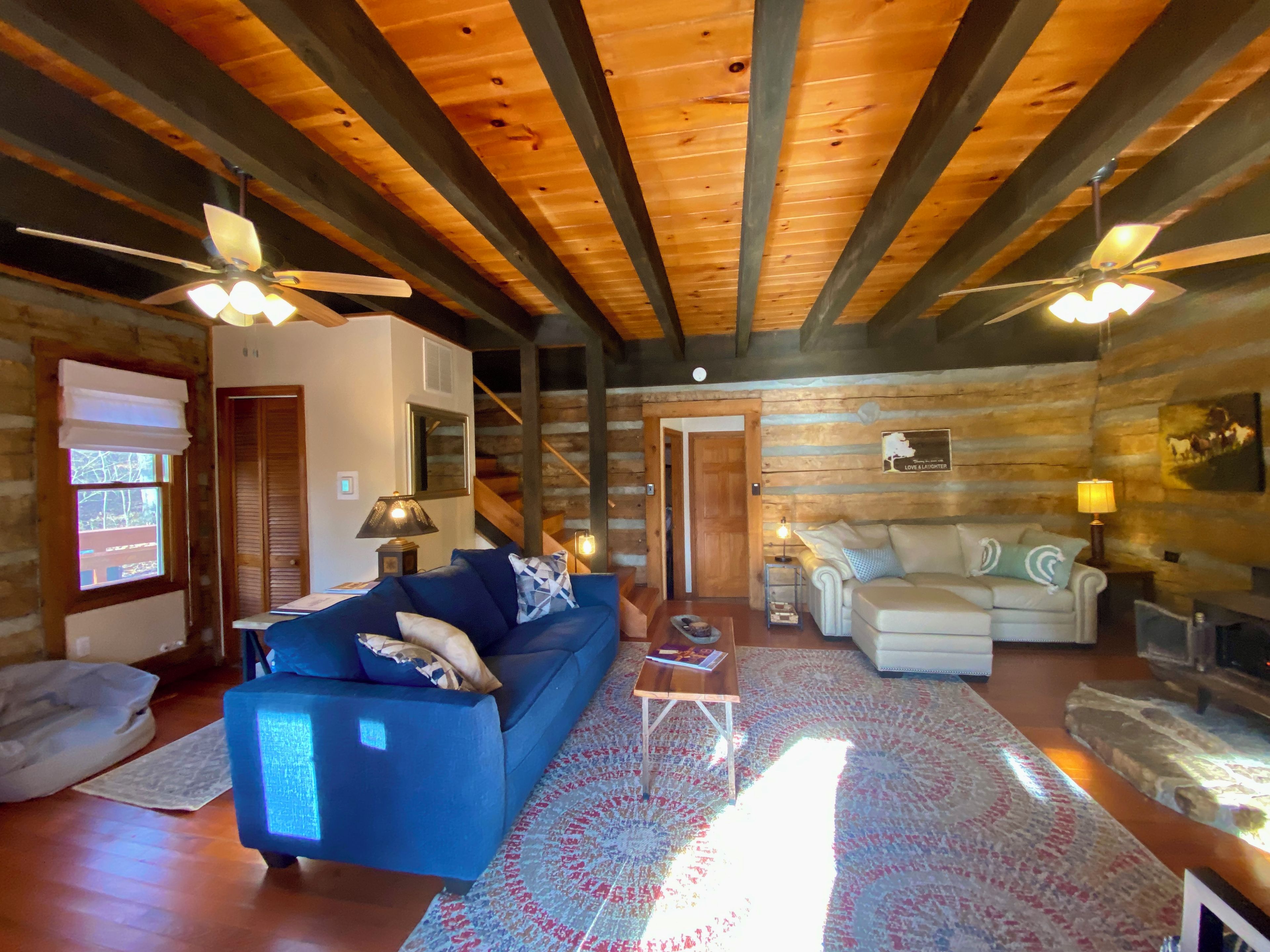 Ein Blockhaushaus-Interieur mit einem blauen Sofa, einem weißen Sessel, einem Kamin und einem Deckenventilator.
