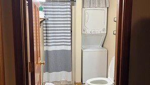 Une petite salle de bain dotée d’un puits de lumière, d’une douche, de toilettes et d’un lave-linge.