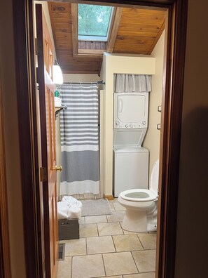 Un baño compacto con tragaluz, ducha, inodoro y lavadora.