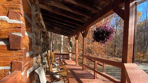 Une terrasse en bois couverte, dotée de chaises et d’une rambarde, qui donne sur une étendue d’eau et est entourée d’arbres.