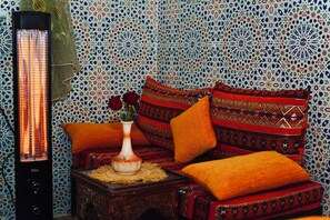 Ein Zimmer mit gemustertem Wanddesign, einem Heizkörper, einer Vase mit Blumen und einem Sofa mit Kissen.