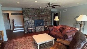 A living room with a stone fireplace, a leather sofa, a coffee table, and a ceiling fan. - Lakefront Luxury: 4BR/4BA Home w/ Massive Seawall Deck (camdenton)