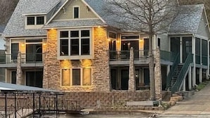 A multi-story house with a stone facade, large windows, and a staircase leading to the upper level. - Lakefront Luxury: 4BR/4BA Home w/ Massive Seawall Deck (camdenton)
