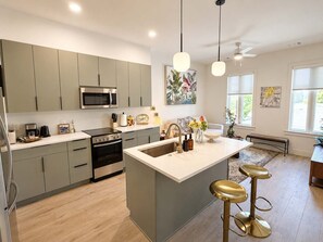 A modern kitchen with grey cabinets, stainless steel appliances, and a central island with stools. - The Jardin Rose Suite | Near Downtown (Savannah)