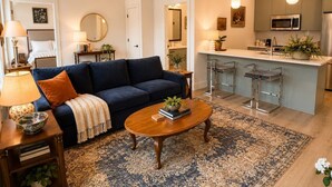 Ein modernes Wohnzimmer mit Sofa, Couchtisch und einer Küchenzeile mit Bar und Geräten.