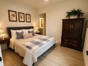 Une chambre à coucher comprenant un lit, des tables de chevet, une commode et des reproductions encadrées de motifs botaniques accrochées au mur.
