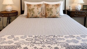 A bed with two floral-patterned pillows, a patterned bedspread, and two bedside tables with lamps. - The Jardin Lily Suite | Near Downtown (Savannah)