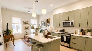 A modern kitchen with a central island, bar stools, a microwave, stove, and various kitchen appliances. - The Jardin Lily Suite | Near Downtown (Savannah)