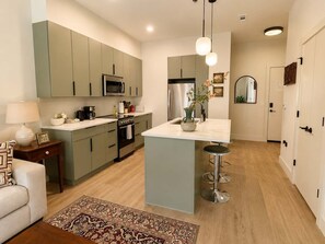 Une cuisine moderne dotée d’un îlot central, d’appareils électroménagers en acier inoxydable et d’un plancher en bois clair.