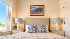 A neatly made bed with a patterned bedspread, two matching pillows, and two bedside lamps. - The Jardin Violet Suite Near Downtown (Savannah)