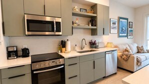 A modern kitchen with a built-in microwave, stove, and oven, a sink, and a countertop with various items. - The Jardin Violet Suite Near Downtown (Savannah)