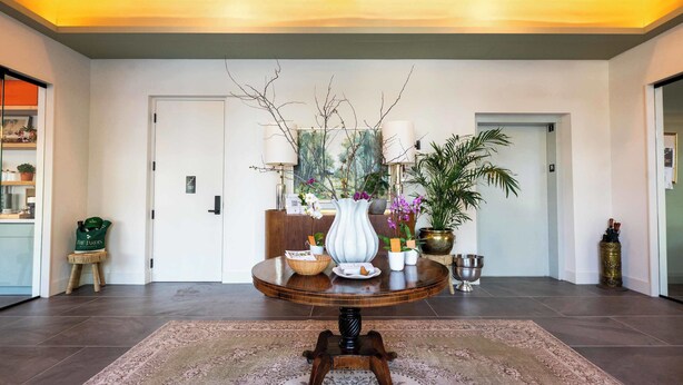 A well-lit room with a round wooden table, a patterned rug, and a door with a painting above it. - The Jardin Violet Suite Near Downtown (Savannah)