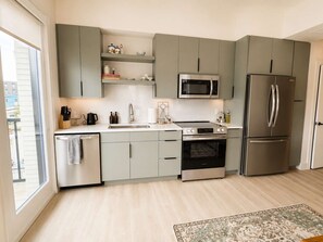 Une cuisine moderne avec des meubles gris, des appareils en acier inoxydable et une vue sur l’extérieur.