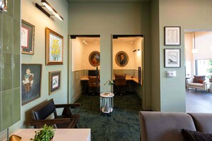 A hotel lobby with framed artwork on the walls, a round table with chairs, and a carpeted floor. - The Jardin Daisy Suite | Near Downtown (Savannah)