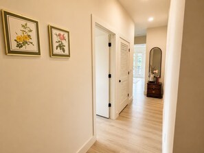 Un pasillo con dos impresiones enmarcadas de motivos botánicos en la pared, una puerta blanca con picaporte negro y un espejo en la pared.