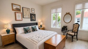 Un dormitorio con cama, mesitas de noche, una silla, un espejo y obras de arte en la pared.